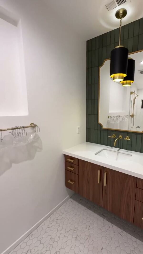 Walnut vanity under a green tile wall and a black pendant light