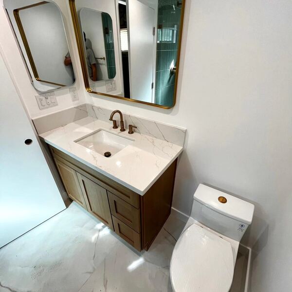 Wood vanity with a quartz top and a brass-framed mirror